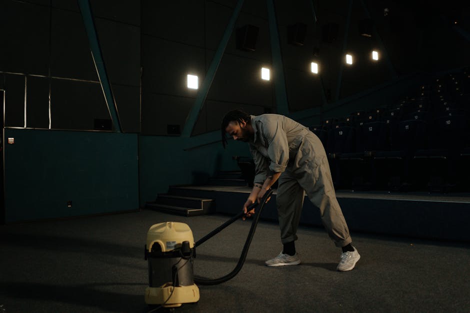 A person wearing black gloves is using a handheld electric polisher on a dark gray fabric sofa cushion in a living room. The sofa has a modern design with a high backrest and wide armrests, situated on a wooden floor. The room features white walls and natural lighting, with a decorated Christmas tree visible on the right side of the image. The scene depicts surface cleaning and maintenance to ensure hygiene and cleanliness of the furniture, in line with professional domestic cleaning services offered by Highbury Carpet Cleaning, as referenced on the Highbury Fields carpet cleaning same day service page.