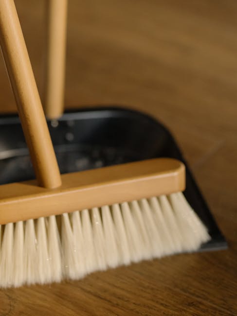 A round black surface on a wooden floor holds cleaning tools including a pair of yellow rubber gloves, a pink microfiber cloth, and a spray bottle with a green cap. The rubber gloves are neatly placed next to the cloth, which appears clean and folded. The spray bottle contains a transparent liquid and is positioned partially inside the gloves. The lighting highlights the shiny, clean surface and the textures of the cloth and gloves, indicating a preparation for surface cleaning or sanitisation. The scene is part of an organized domestic cleaning setup, emphasizing hygiene and thorough cleaning practices, with the highburycarpetcleaning.com branding and the context related to understanding hidden cleaning charges in Highbury.